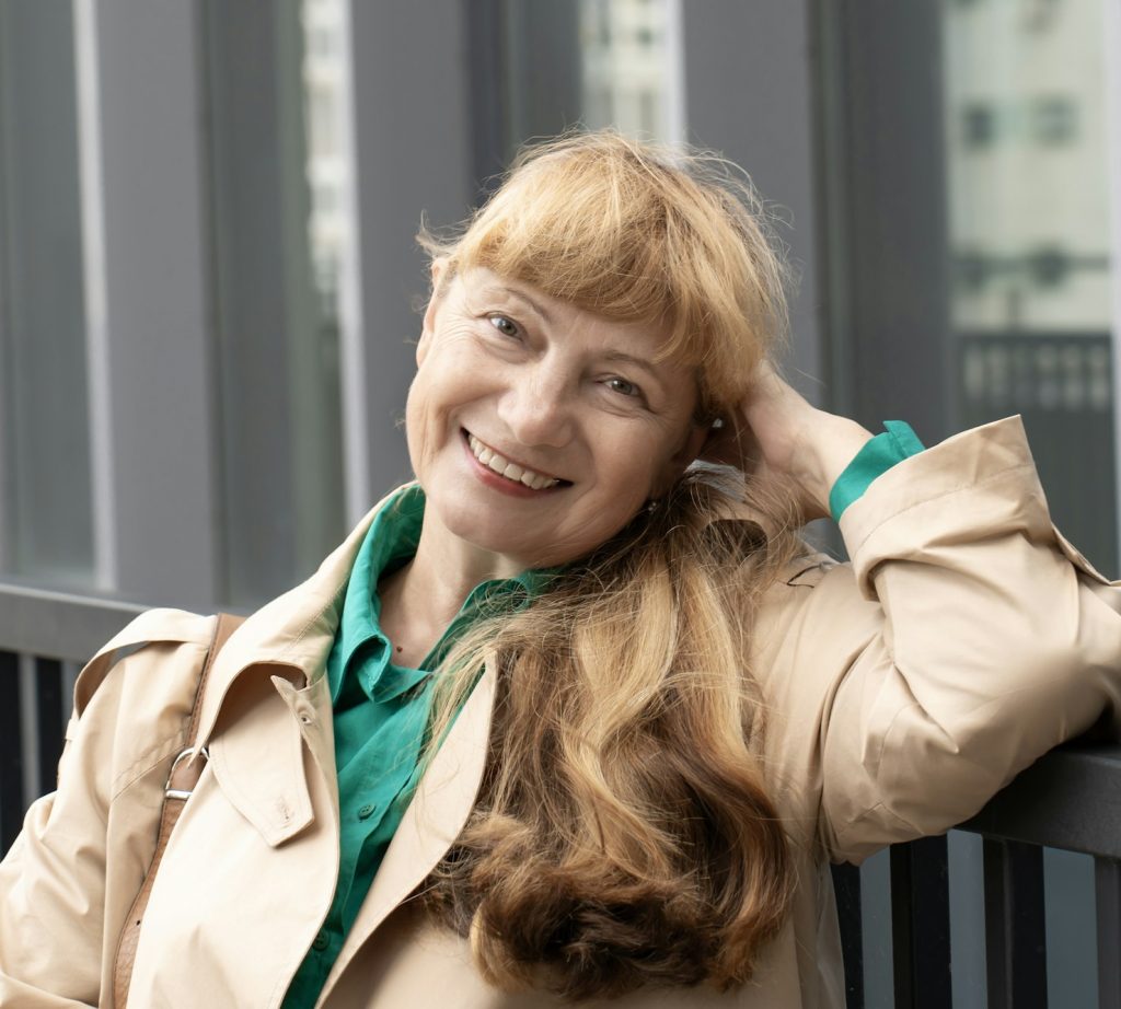 A 60-year-old woman in a beige raincoat walks among tall buildings. Woman enjoying life